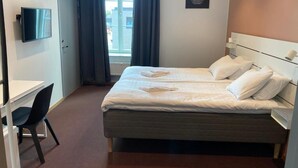 A hotel room with a bed, a desk, a chair, a television, and a window with curtains. - Ahlgrens Hotell Bed & Breakfast (Gävle)