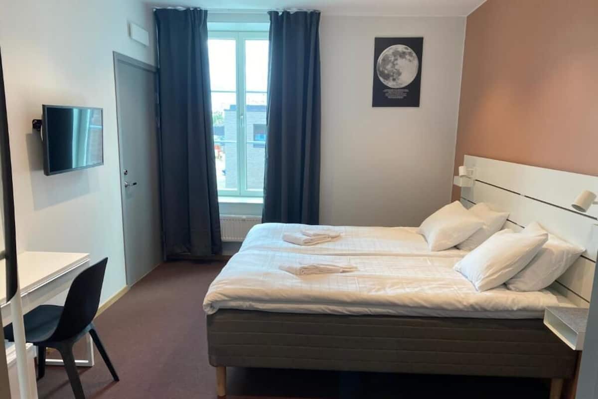 A hotel room with a bed, a desk, a chair, a television, and a window with curtains.