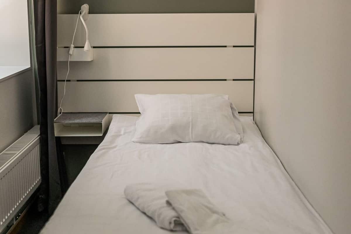 A single bed with white bedding, a bedside table with a lamp, and a radiator.