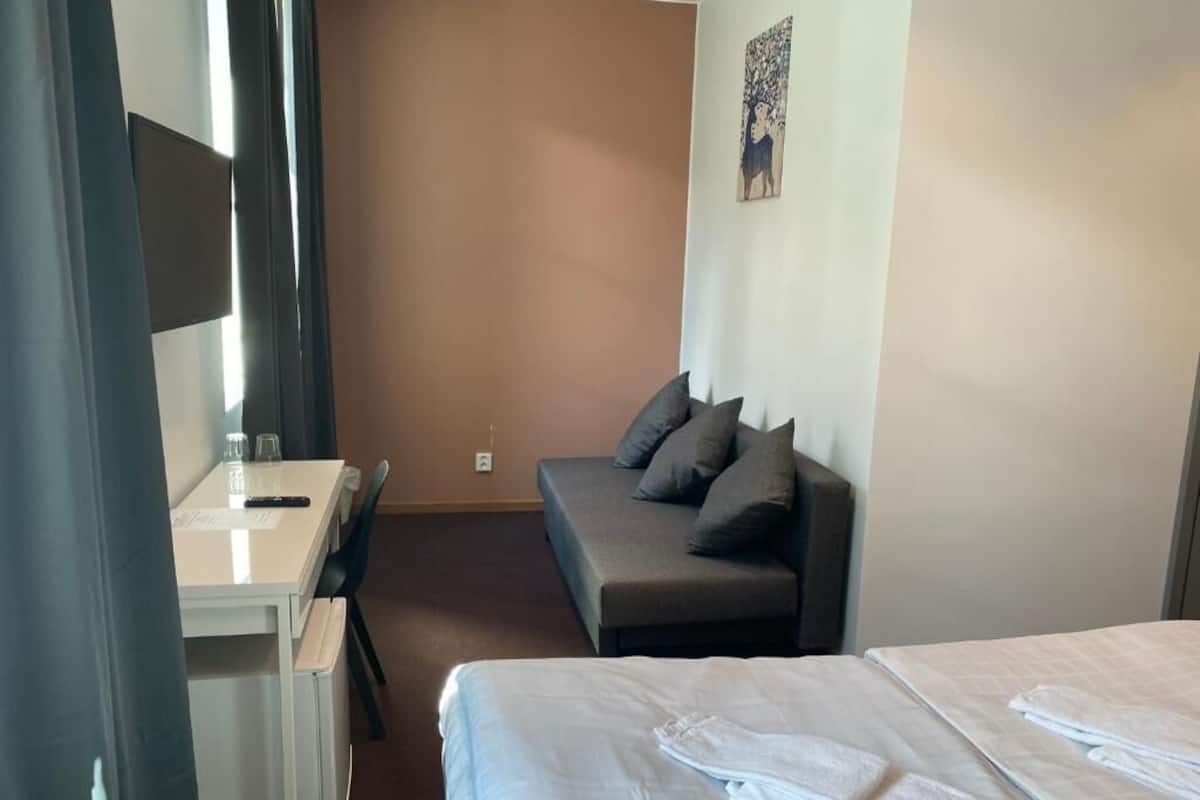 A hotel room with a bed, a sofa, a desk with a chair, and a small table with a remote control.