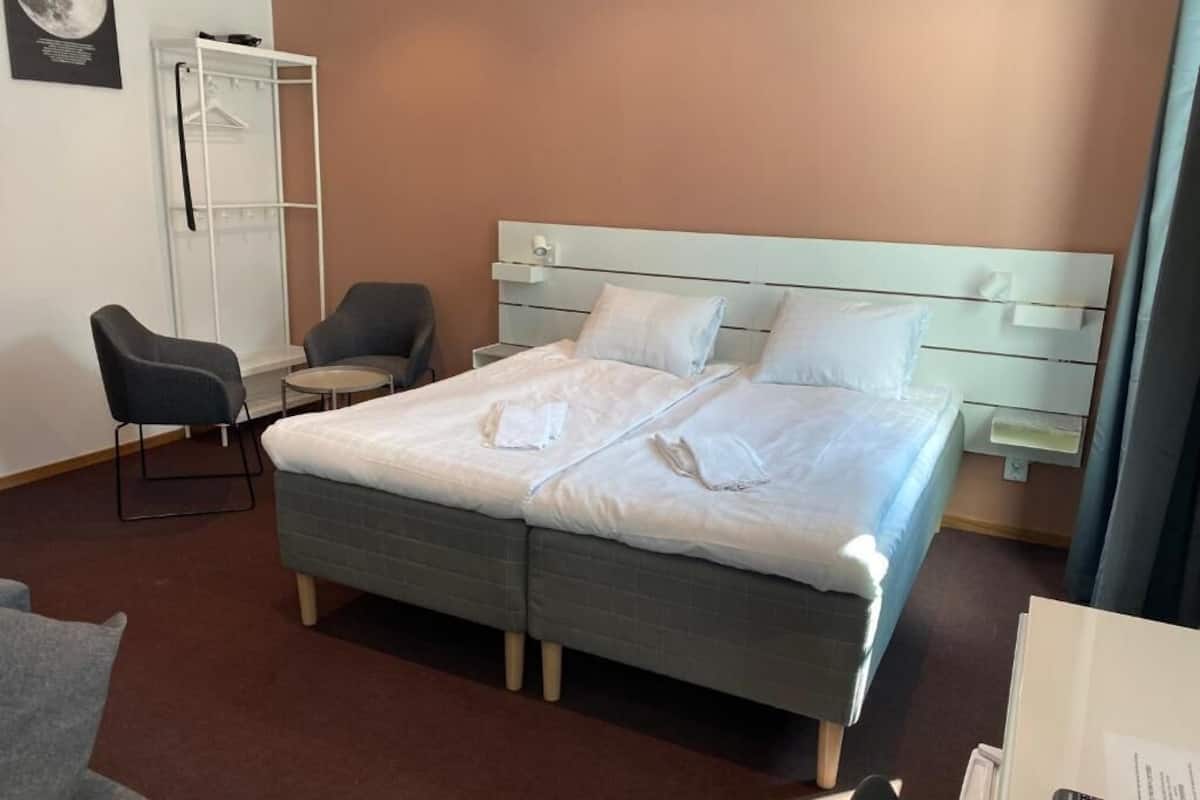 A hotel room with a double bed, two bedside tables, a wardrobe, and a chair.