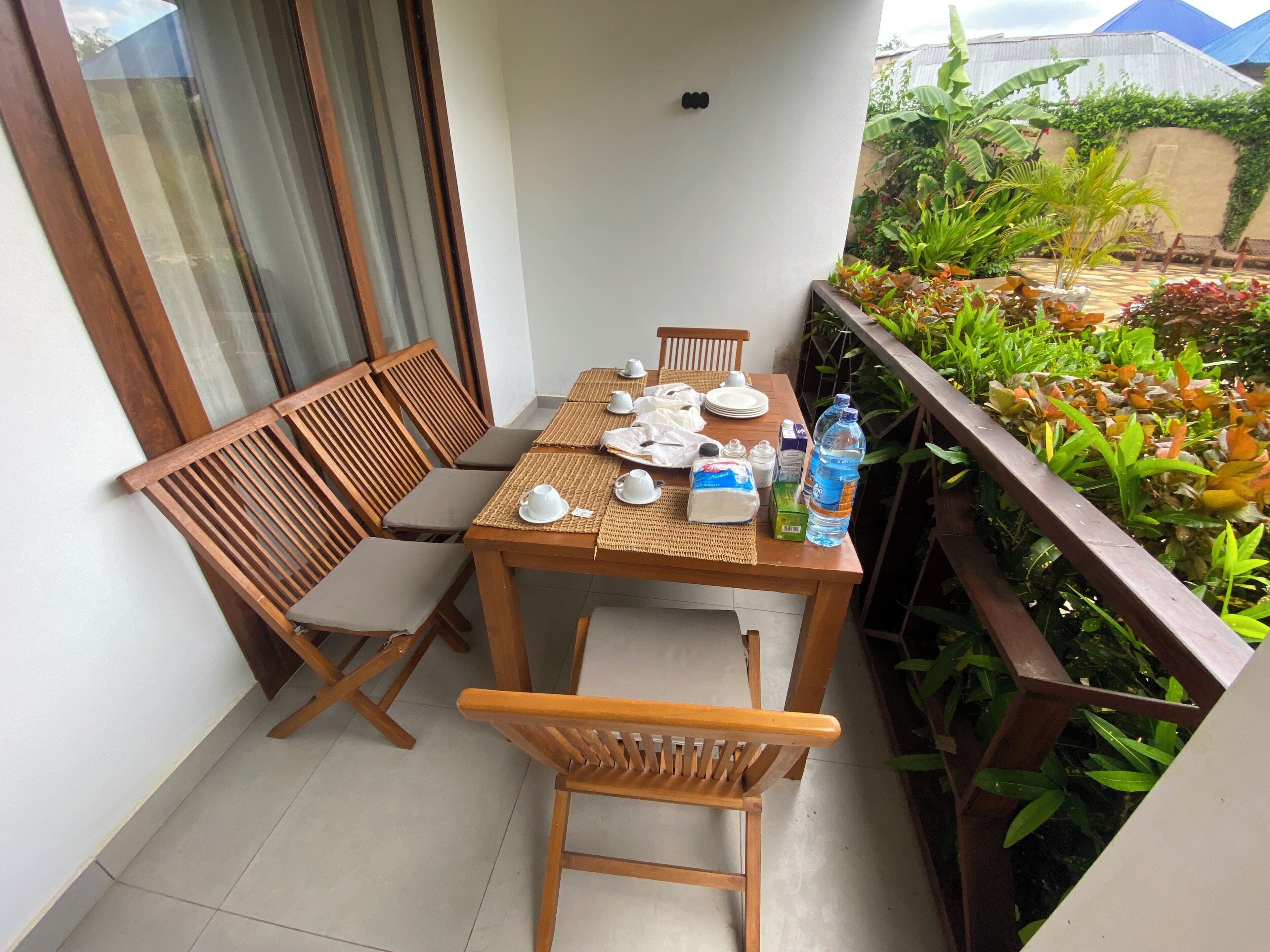 Een balkon met een houten tafel, gedekt voor thee, omringd door stoelen en een waterfles.