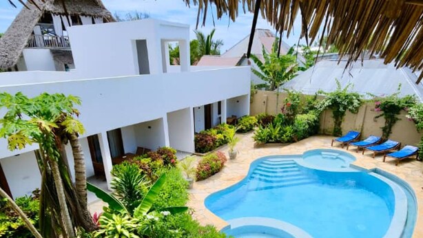 A pool area with a clear blue pool, surrounded by lush greenery and palm trees. - The Dream Village (Kiwengwa)