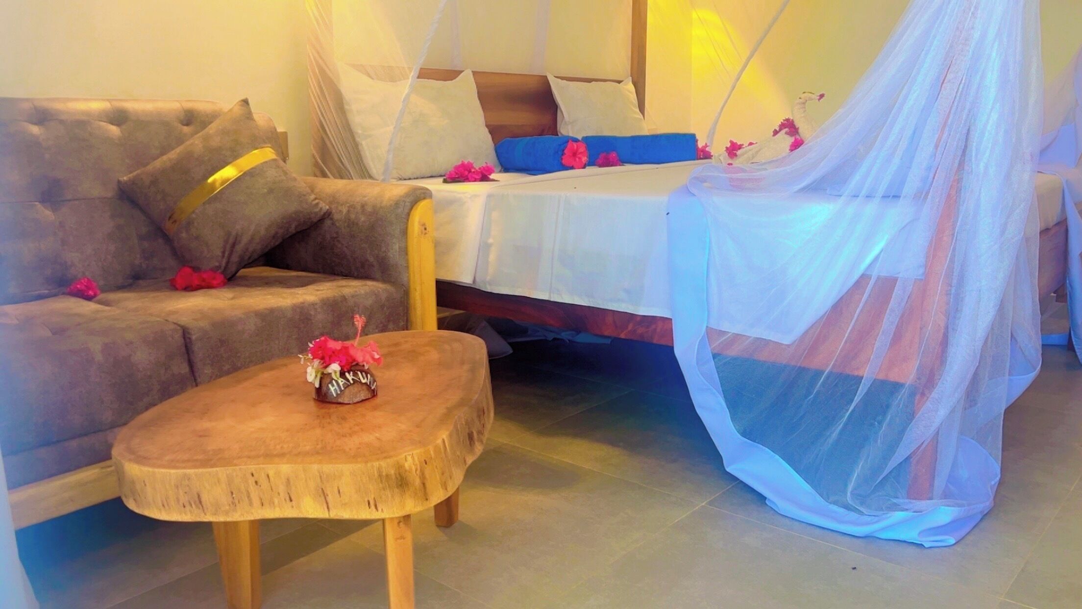 Une chambre avec un lit, un canapé, une petite table en bois et une moustiquaire.