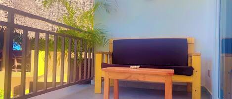 A balcony with a wooden bench and a small table, a railing, and a palm tree.