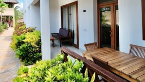 A white building with wooden beams, a patio with a table and chairs, and a thatched-roof structure in the background. - The Dream Village (Kiwengwa)