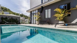 Una piscina con agua azul cristalina, rodeada por un edificio moderno con amplios ventanales y plantas en macetas.