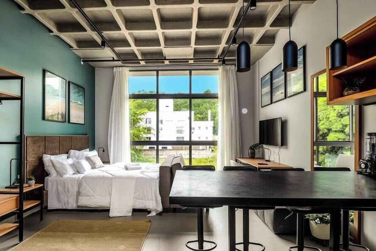 A modern bedroom with a bed, bedside tables, a desk, and a large window.