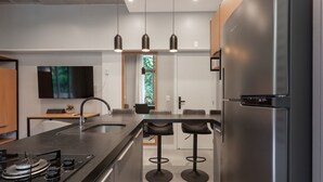 Uma cozinha moderna com geladeira de aço inoxidável, fogão a gás embutido, TV de tela plana na parede e uma grande janela com vista para o verde.