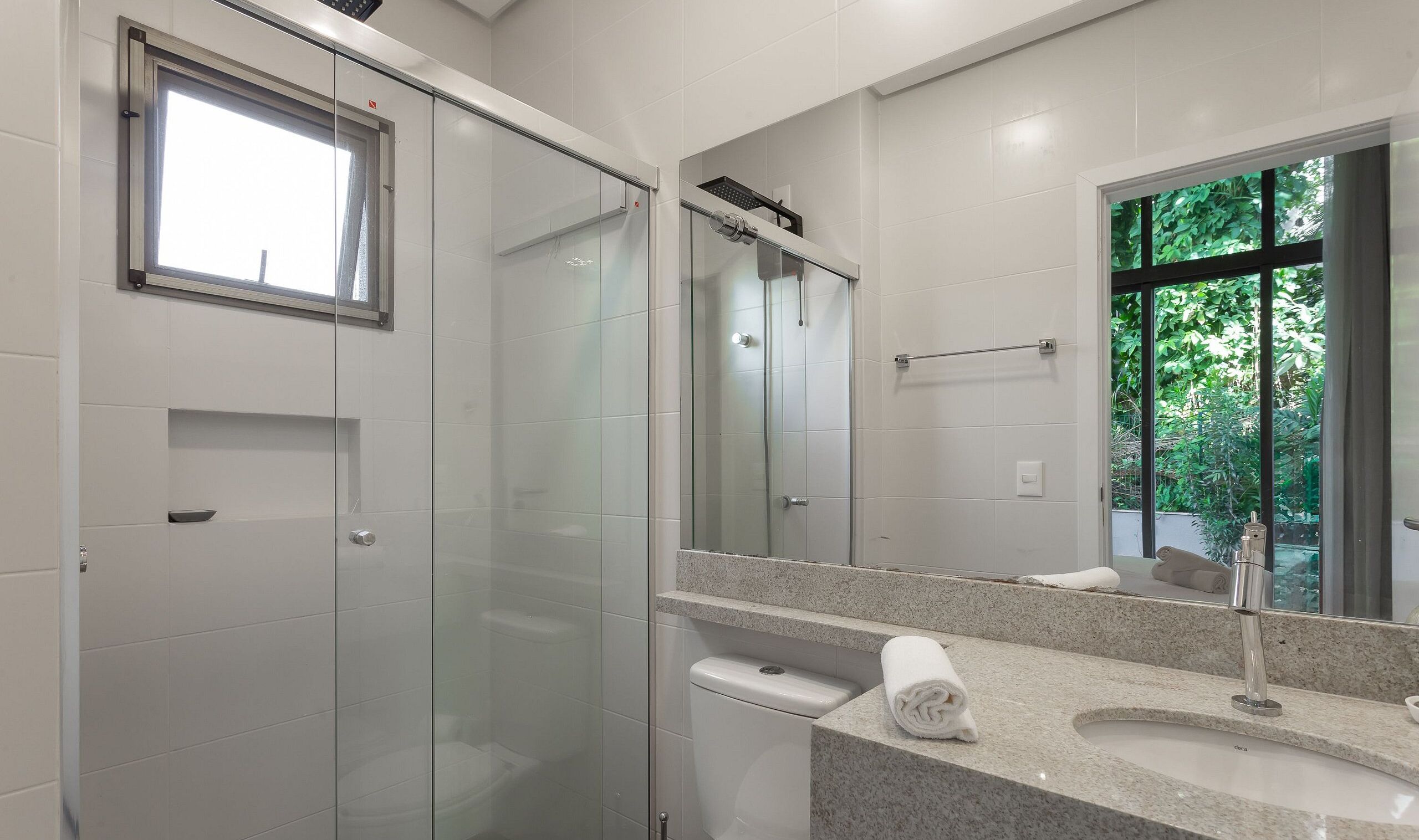 Een moderne badkamer met een douche met glazen wand, een grote spiegel en een wastafel met een handdoek.