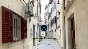 Una calle estrecha flanqueada por edificios, con contraventanas tradicionales y un cielo azul despejado.