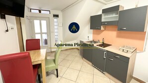 Una cocina moderna con armarios grises, encimera de madera y un lavamanos. Hay una zona de comedor con una silla roja y una silla verde.