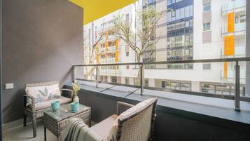 Un balcone con mobili in vimini, un vaso con fiori e vista su un edificio moderno con balconi.