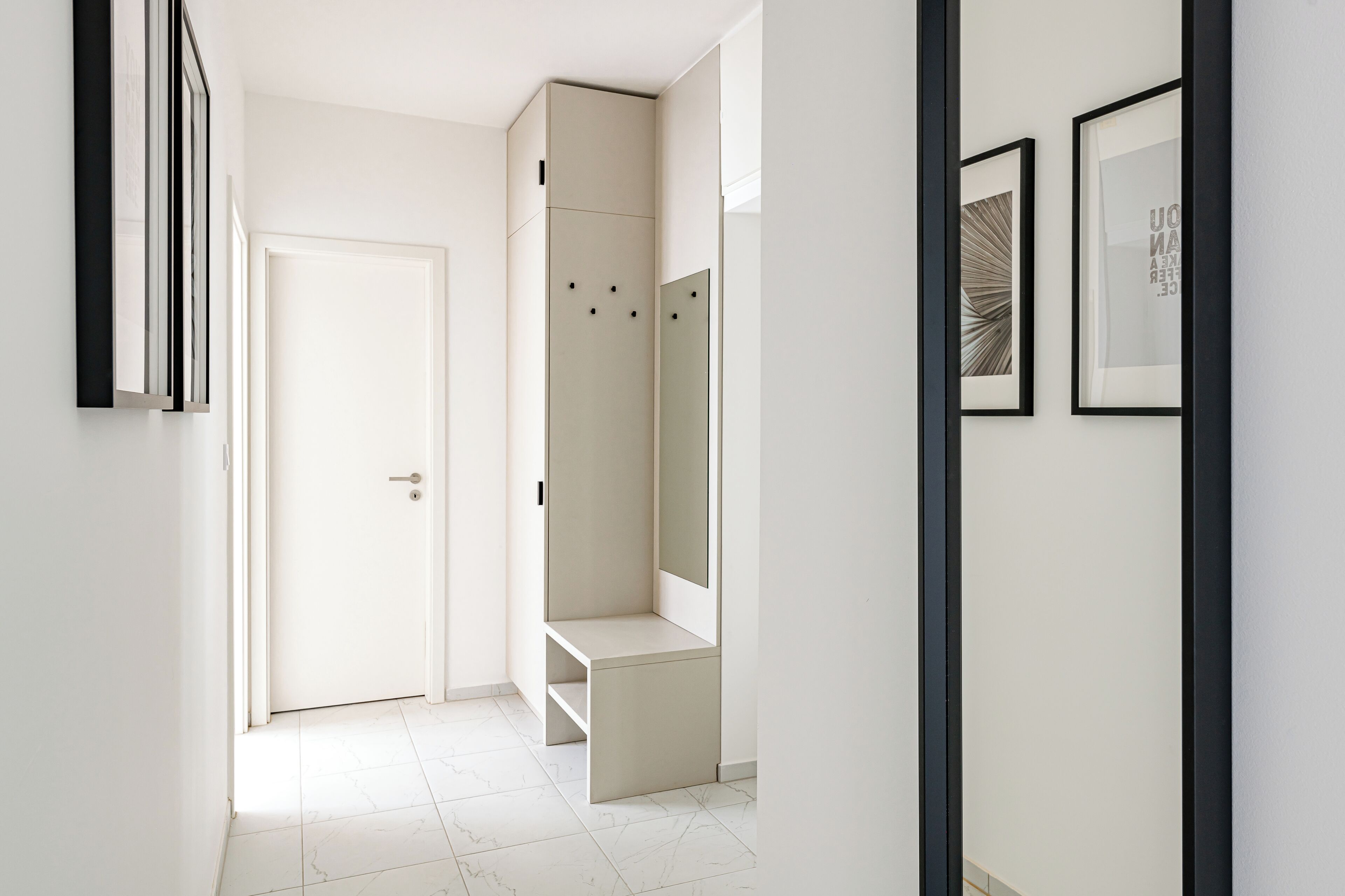 A hallway with a white door, a built-in bench, and framed artwork on the walls.