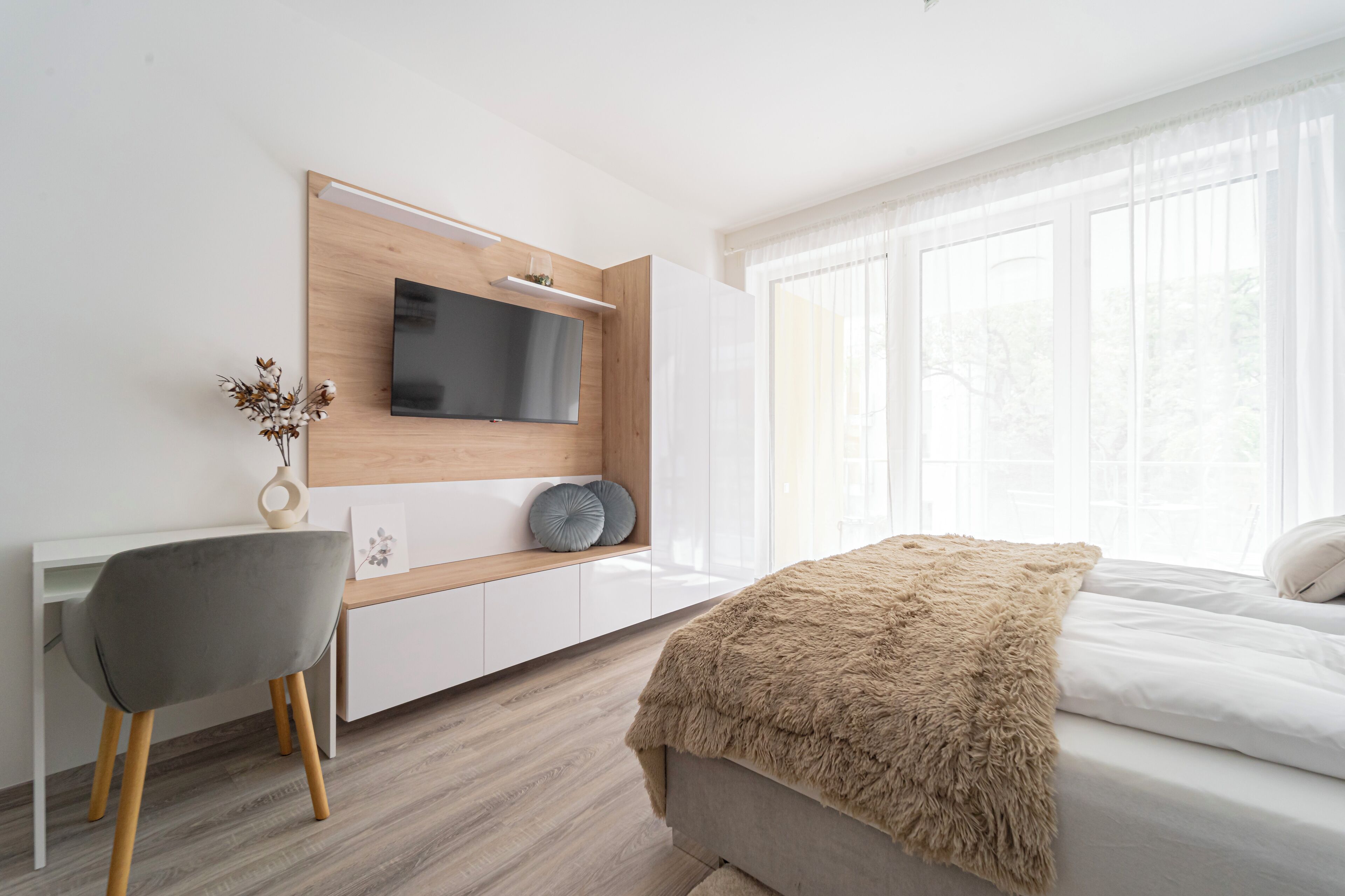 A modern bedroom with a bed, a desk, and a TV mounted on a wooden panel.