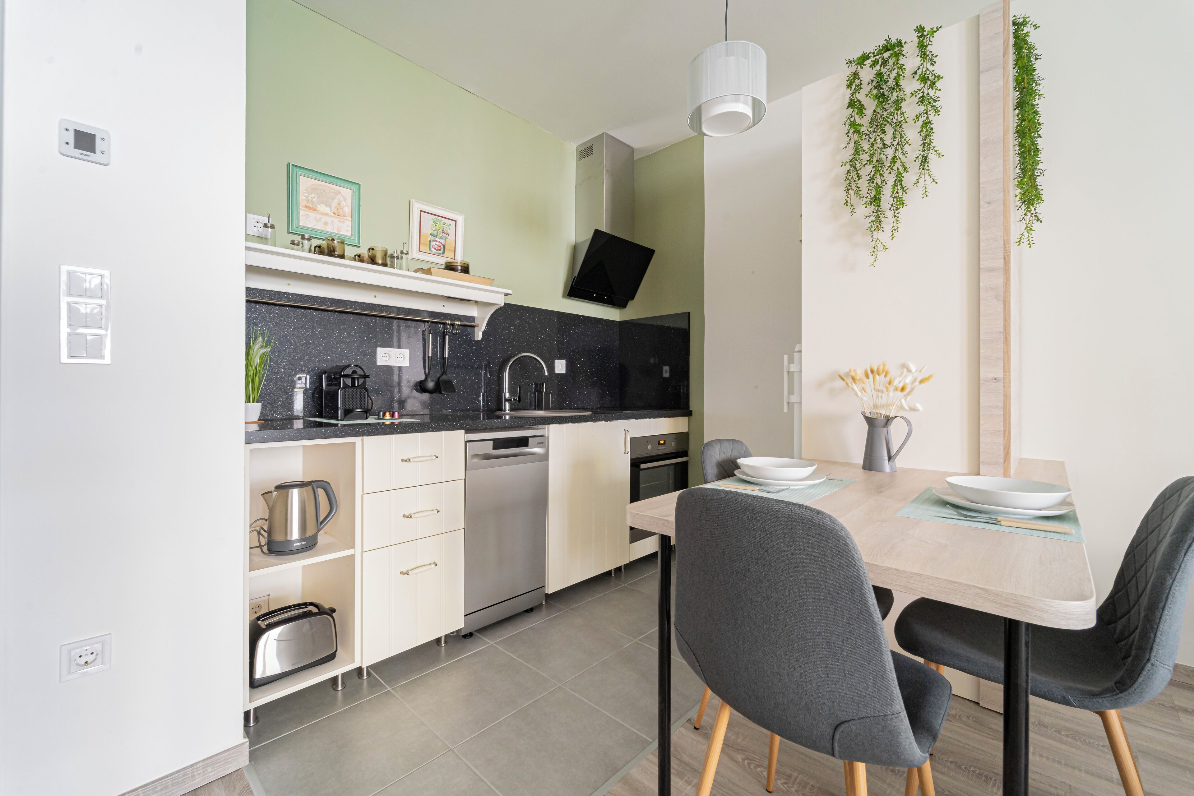 A modern kitchen with white cabinets, a black countertop, and a dining area with a wooden table and two chairs.