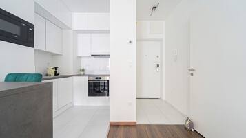 Uma cozinha moderna com armários brancos, forno embutido e bancada cinzenta.