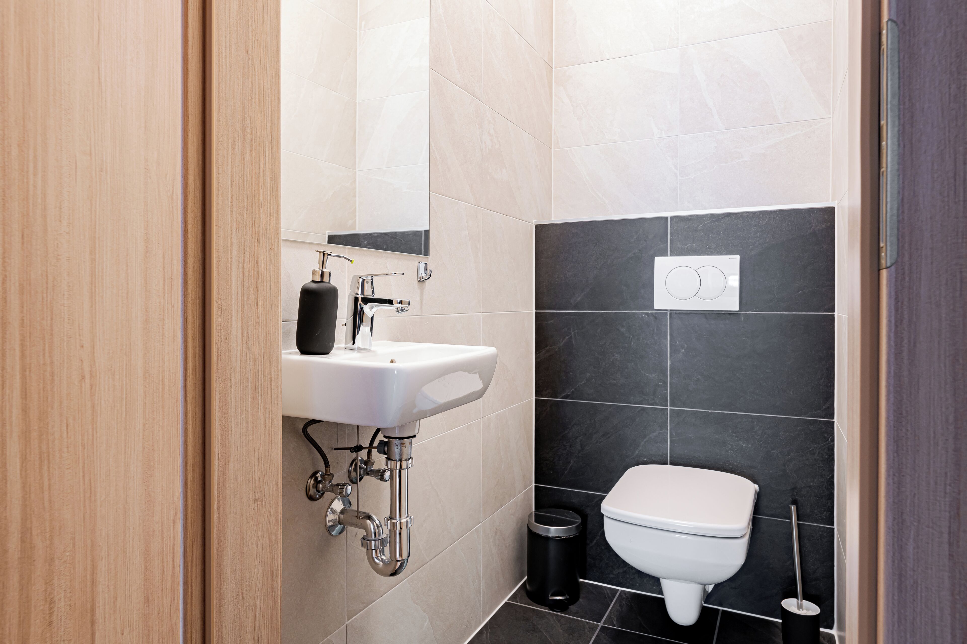 Un baño moderno con un lavabo blanco, baldosas negras y un inodoro blanco.