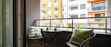 Un balcón con mesa y sillas, vista a un edificio de varios pisos también con balcones, y un techo amarillo.