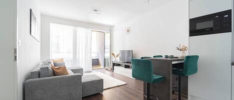 A modern living room with a grey sofa, teal bar stools, and a dining area with a white table and chairs.