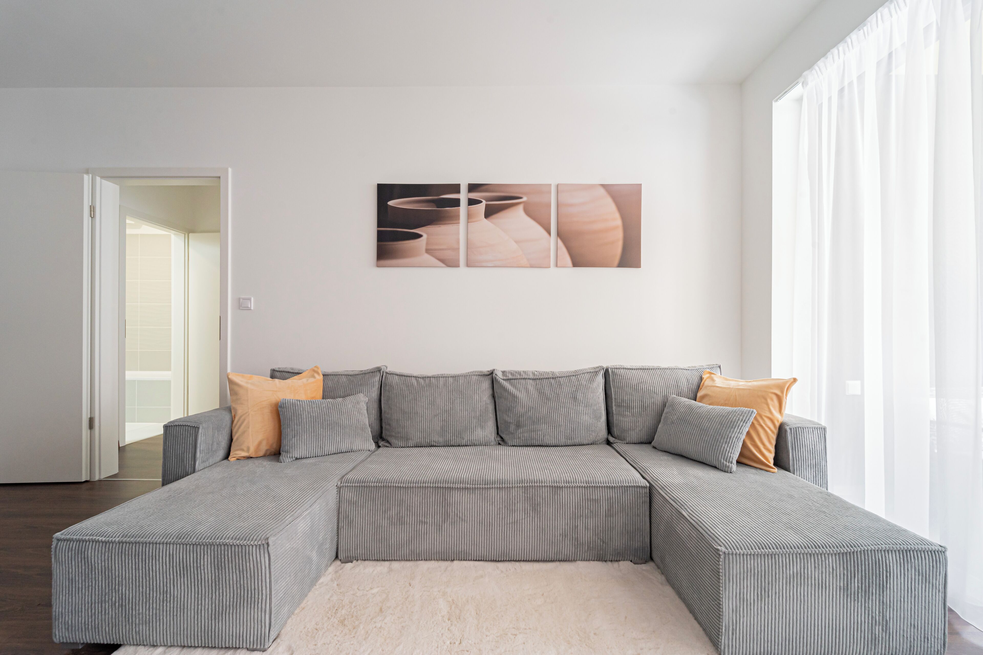 A modern living room with a grey sectional sofa, a white rug, and a wall-mounted artwork.