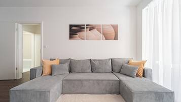 A modern living room with a grey sectional sofa, a white rug, and a wall-mounted artwork.