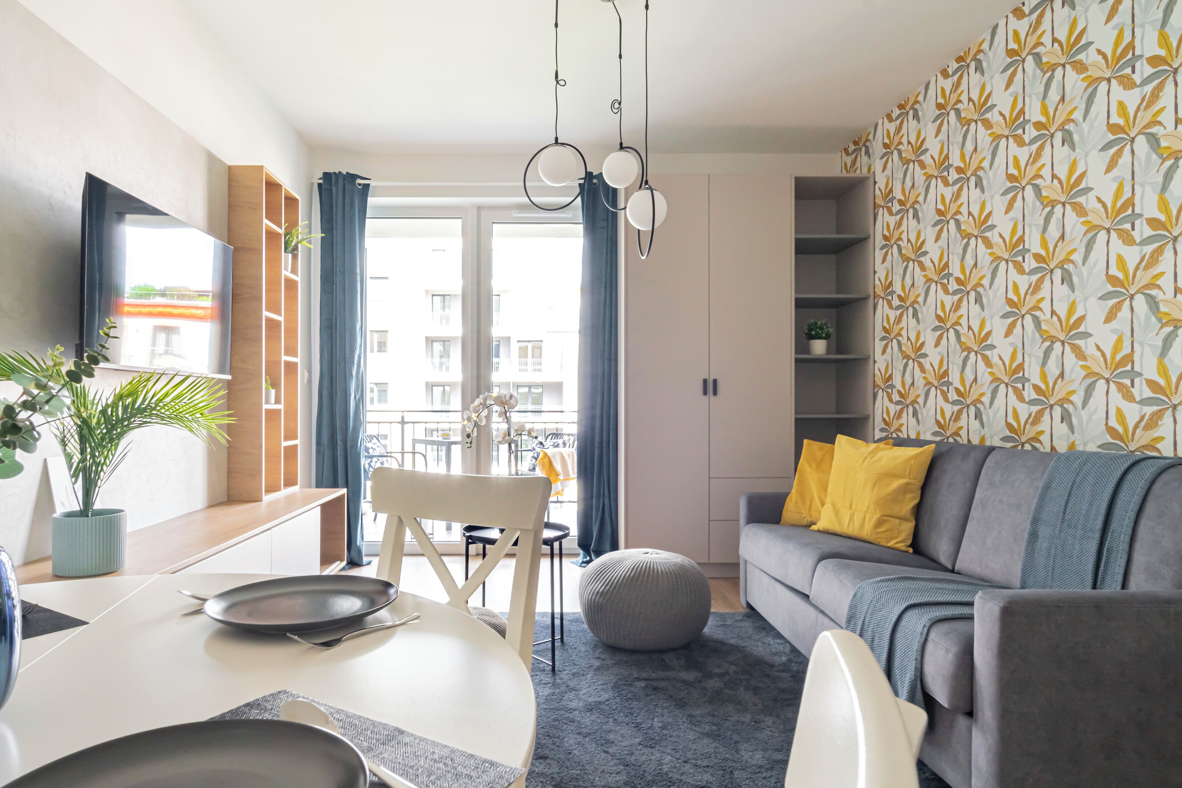 Un salon moderne avec un canapé gris, une table à manger et des chaises, ainsi qu’un balcon offrant une vue sur les immeubles.