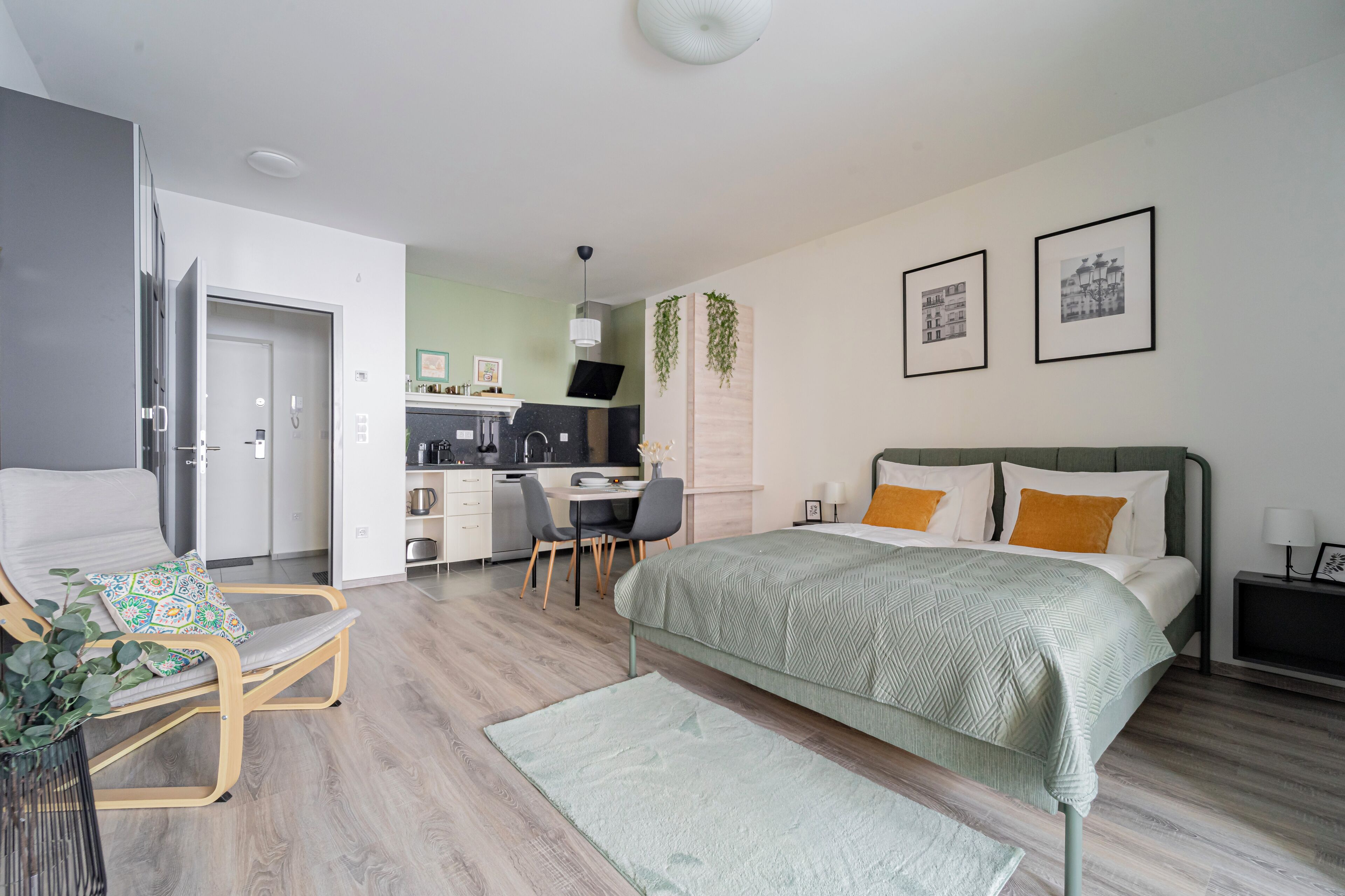 Un dormitorio moderno con cama, escritorio y silla. Se observa una kitchenette al fondo.