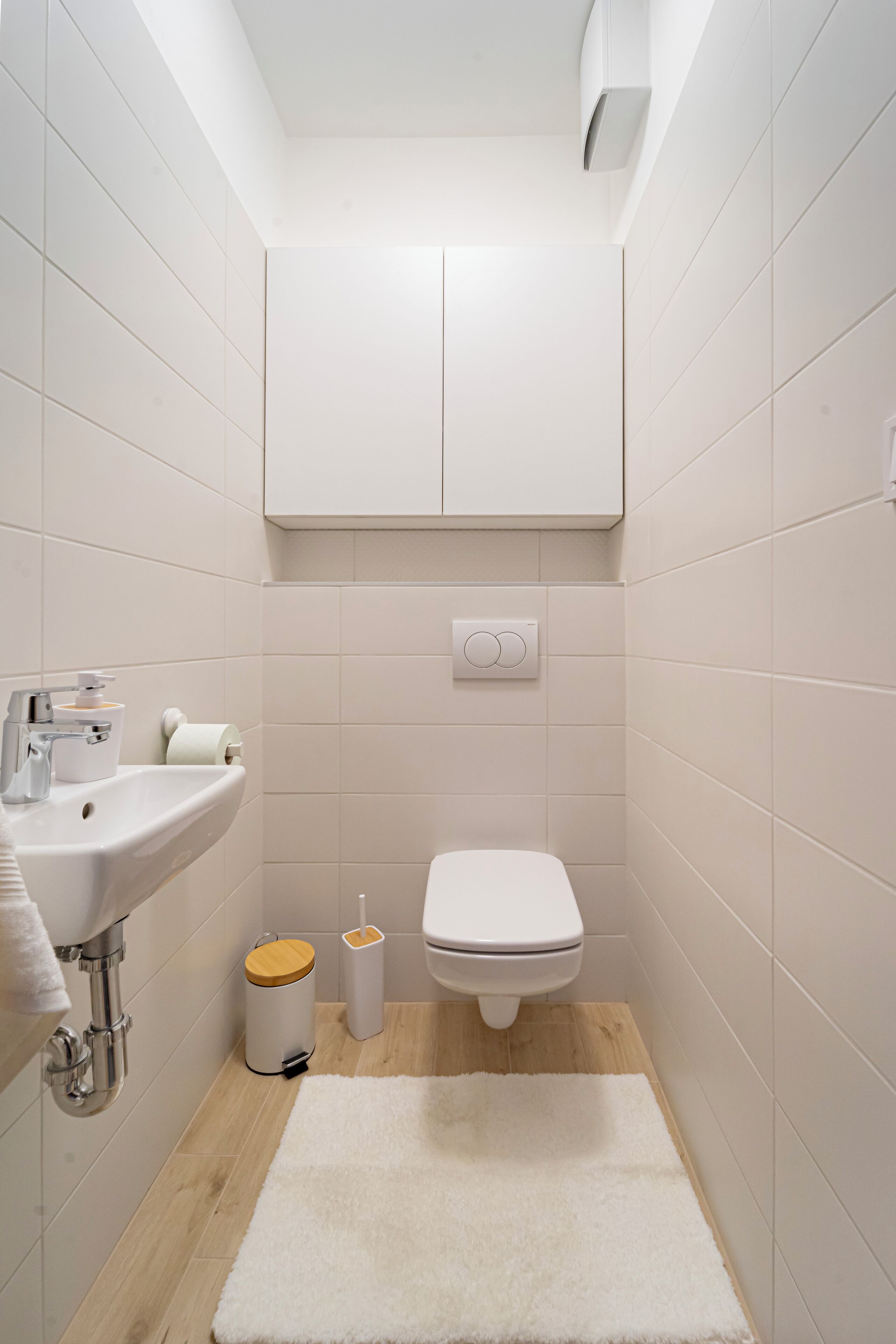 Een compacte, moderne badkamer met een witte wastafel, toilet en een houten vloer.