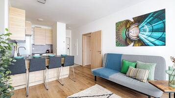 Uma sala de estar moderna com um sofá cinzento, uma mesa de centro e um espaço de jantar, com uma cozinha ao fundo.
