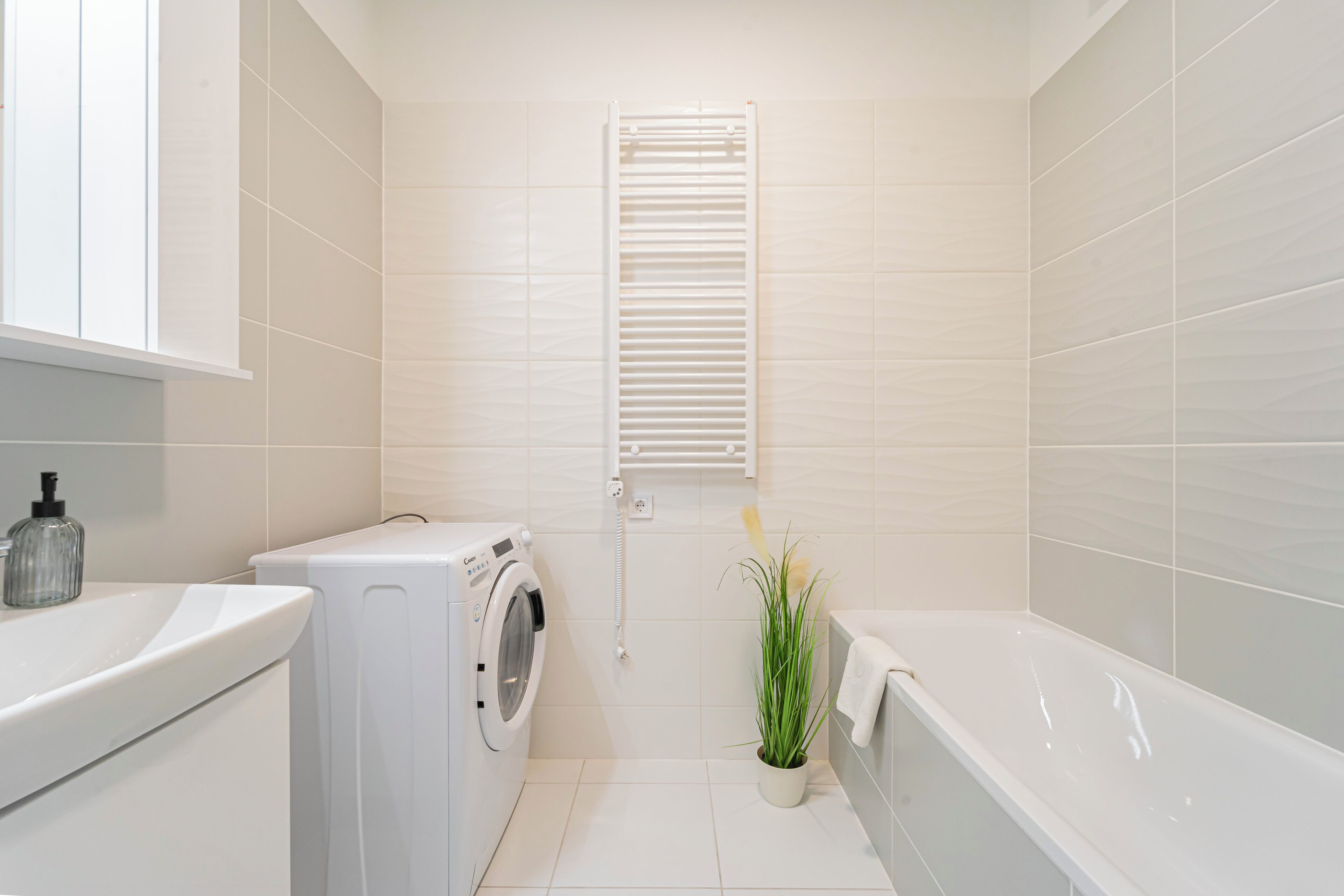 Une salle de bain moderne équipée d’un lave-linge, d’un évier, d’une baignoire et d’une fenêtre avec des stores.