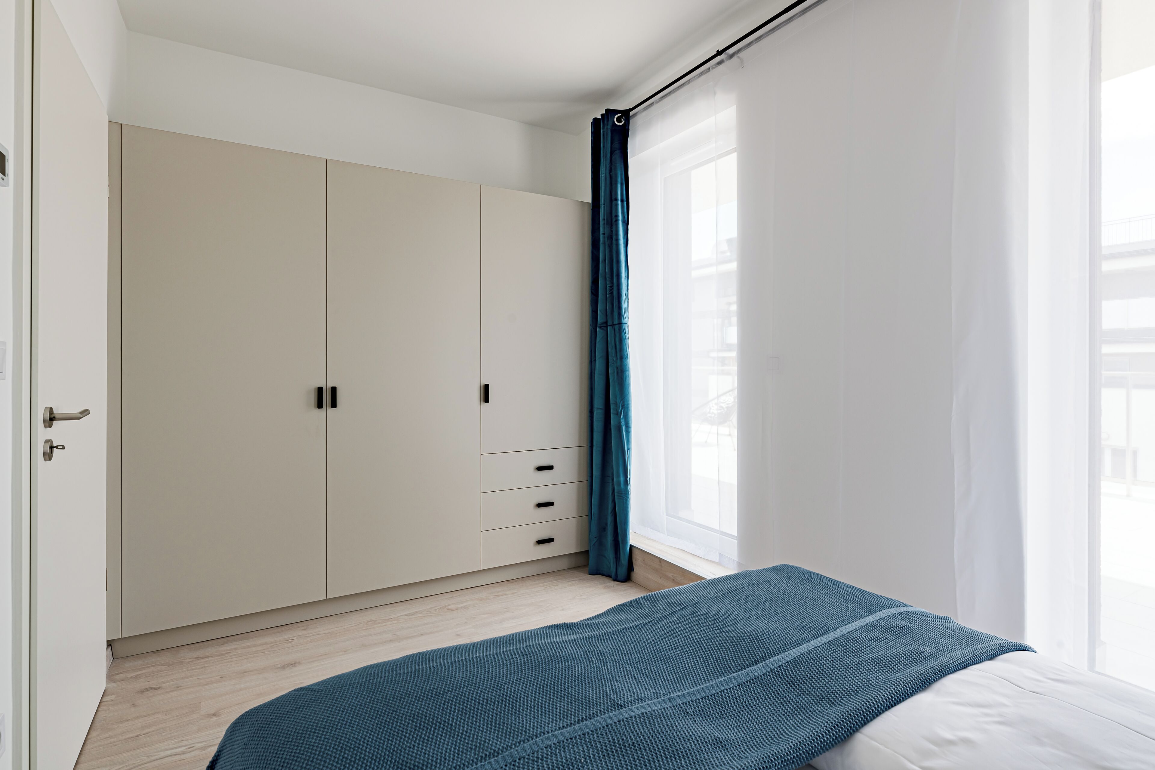 Un dormitorio con cama, armario y ventana con cortinas.