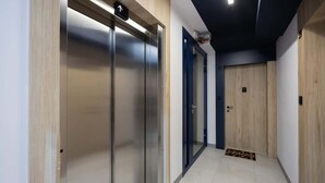 Um corredor moderno com elevador metálico, uma porta azul e uma porta de madeira.