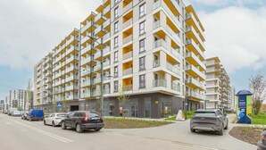Um edifício residencial moderno de vários andares, com varandas, área de estacionamento e céu claro.