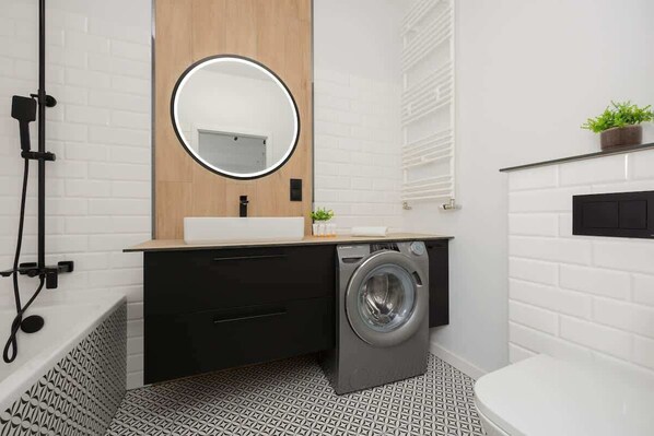 Un baño moderno con lavadora, lavabo con espejo y retrete.