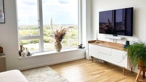 A modern living room with a large window, a flat-screen TV, a wooden cabinet, and a potted plant. - Modern Apartment with a View

 (København)