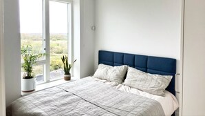 A bedroom with a large window, a bed with a blue headboard, and a potted plant on the windowsill. - Modern Apartment with a View

 (København)