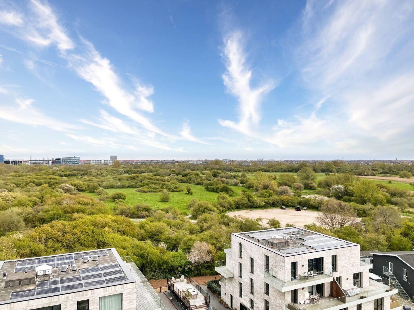 A modern building with a rooftop solar panel array, surrounded by lush greenery and a clear sky.