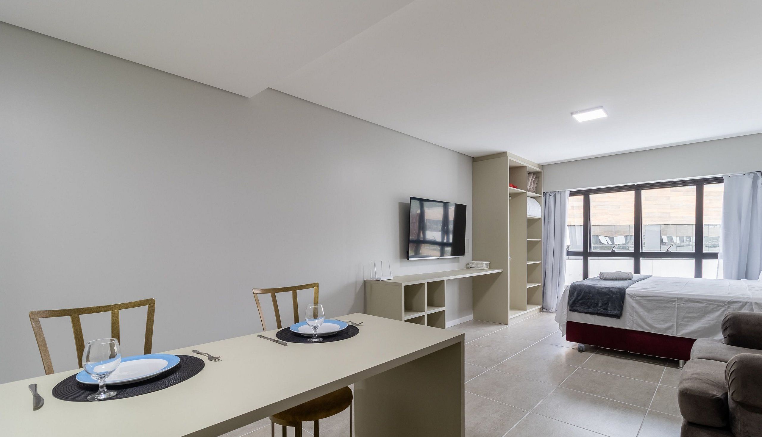 Et moderne hotelværelse med spiseplads, seng, fjernsyn og et stort vindue.