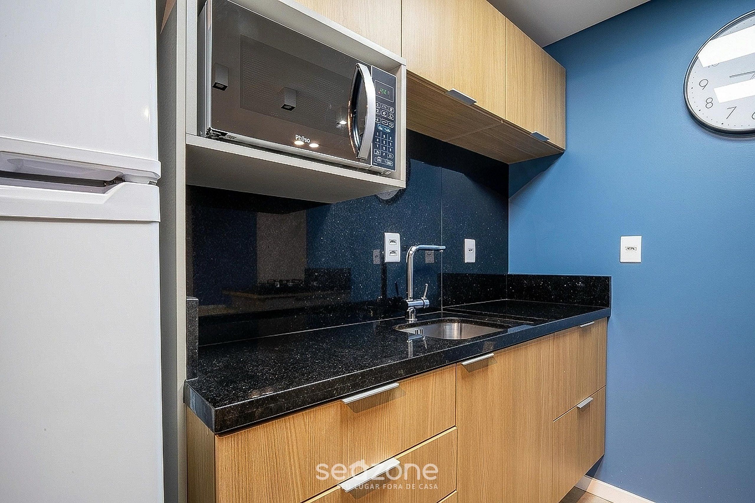 A kitchen with a microwave, sink, and wooden cabinets.
