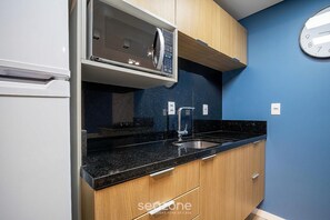 A kitchen with a microwave, sink, and wooden cabinets. - OKA Floripa (Florianópolis)