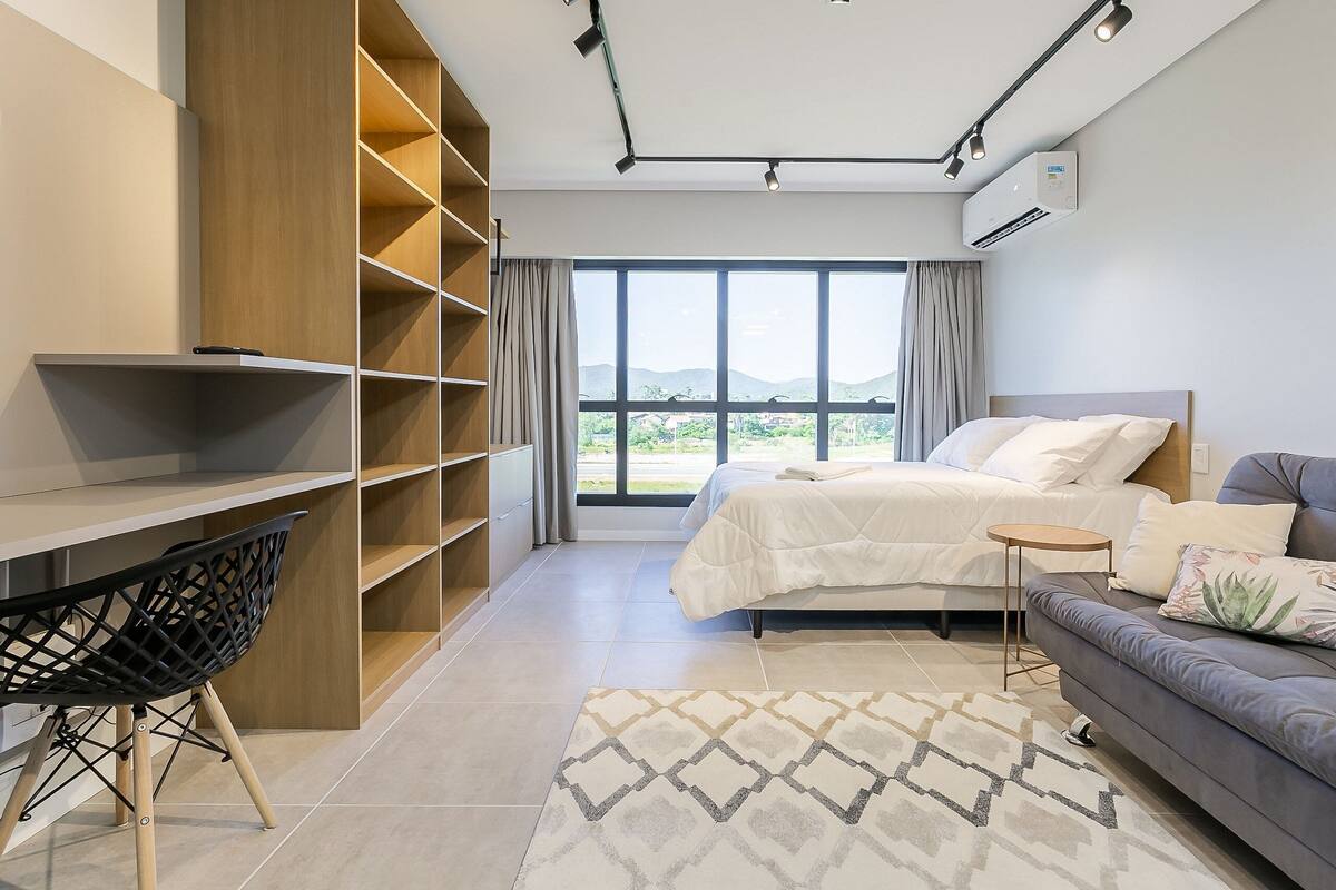Une chambre d’hôtel moderne équipée d’un lit, d’un canapé, d’un bureau et d’une grande fenêtre donnant sur un paysage agréable.