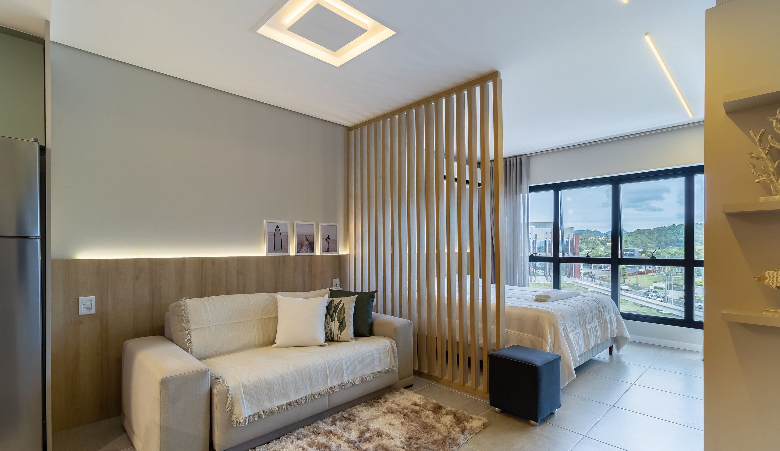 A modern bedroom with a sofa, a bed, a view through large windows, and a decorative wall panel.