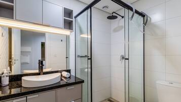 Un baño moderno con cabina de ducha de vidrio, tocador curvo con lavabo blanco y un espejo grande.