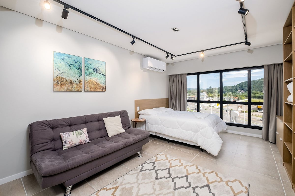 Une chambre moderne avec un canapé, un lit, une petite table de chevet et une grande fenêtre donnant sur un beau paysage.