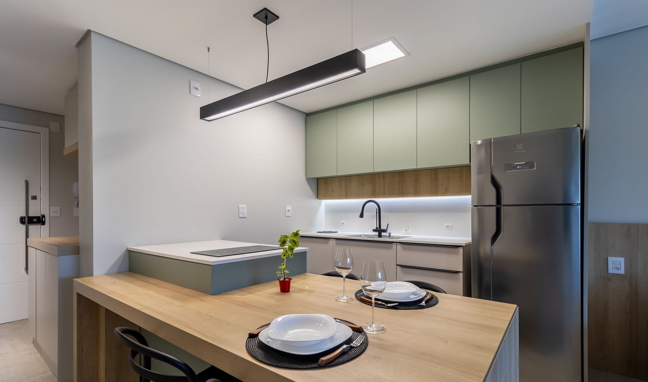A modern kitchen with a wooden countertop, a built-in oven, a stainless steel refrigerator, and a pendant light.