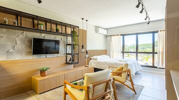 A modern bedroom with a large window, a bed, a TV, and a seating area with a plant.