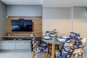 A modern dining area with a TV, wooden paneling, and floral-patterned chairs. - OKA Floripa (Florianópolis)