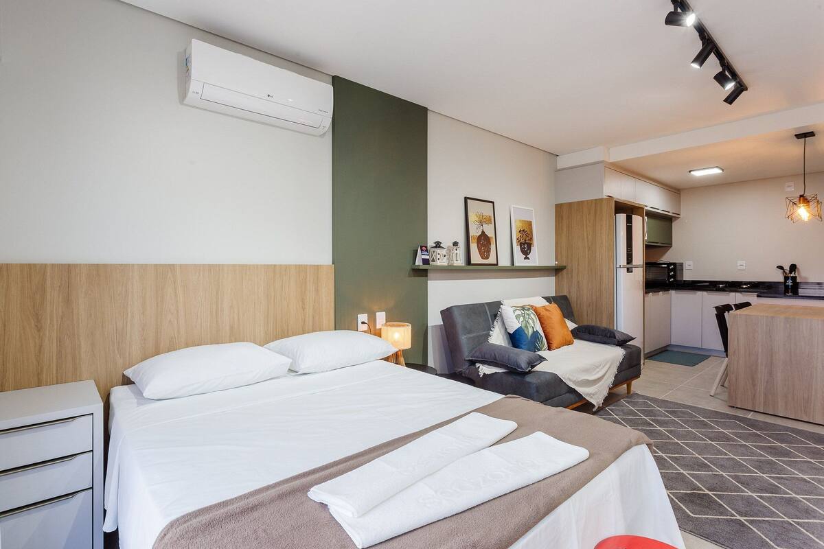 Une chambre d’hôtel équipée d’un lit, d’un bureau, d’une chaise, d’une kitchenette et d’un luminaire suspendu.