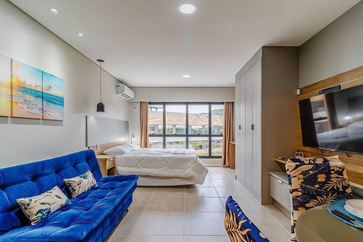 Une chambre d’hôtel avec un lit, un canapé bleu, une télévision et une grande fenêtre donnant sur un beau paysage.